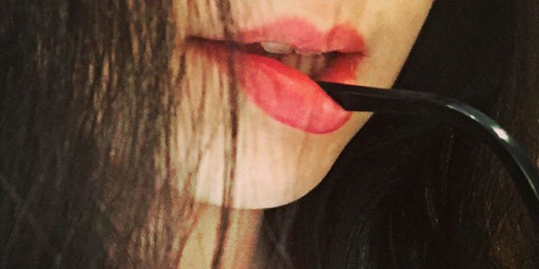 Labios de boca de mujer sujetando sensualmente unas gafas de sol