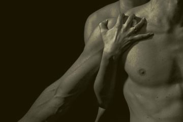 torso de un hombre iluminado en la oscuridad con manos recorriendo su pecho