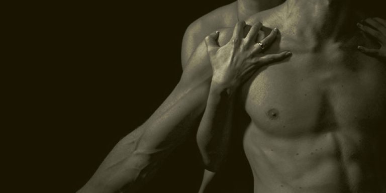 torso de un hombre iluminado en la oscuridad con manos recorriendo su pecho
