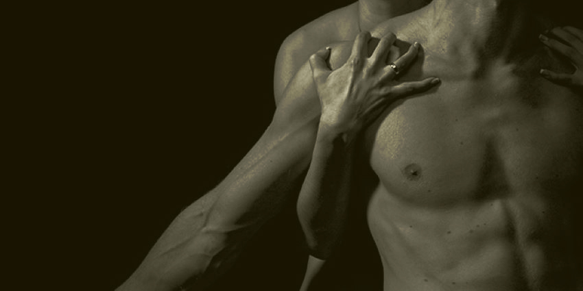 torso de un hombre iluminado en la oscuridad con manos recorriendo su pecho