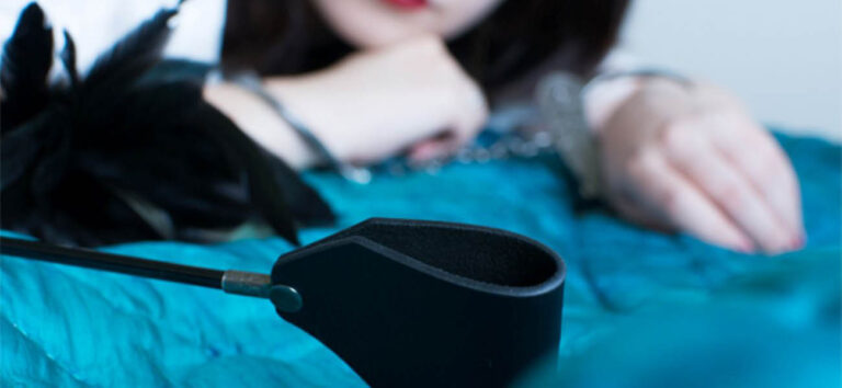 Esposas y fusta sobre una cama junto a una mujer en una escena de cuff bondage y BDSM lésbico