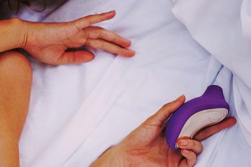 persona sosteniendo un succionador de clítoris en la cama