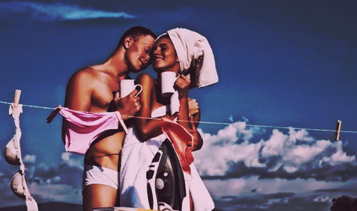 Pareja sonriente compartiendo un momento íntimo en casa mientras tienden la ropa