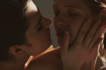 dos mujeres a punto de besarse en una escena íntima iluminada por luz cálida