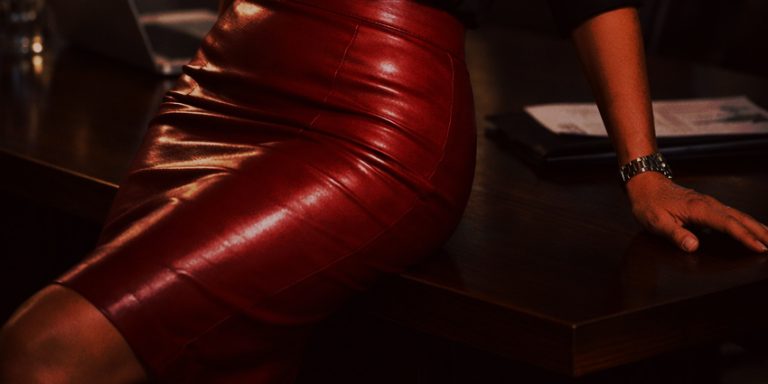 Ejecutiva apoyada en mesa de reuniones con falda de cuero rojo en oficina moderna.