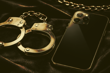 Smartphone y esposas metálicas sobre superficie de terciopelo oscuro con iluminación dramática, concepto de apps BDSM seguras.