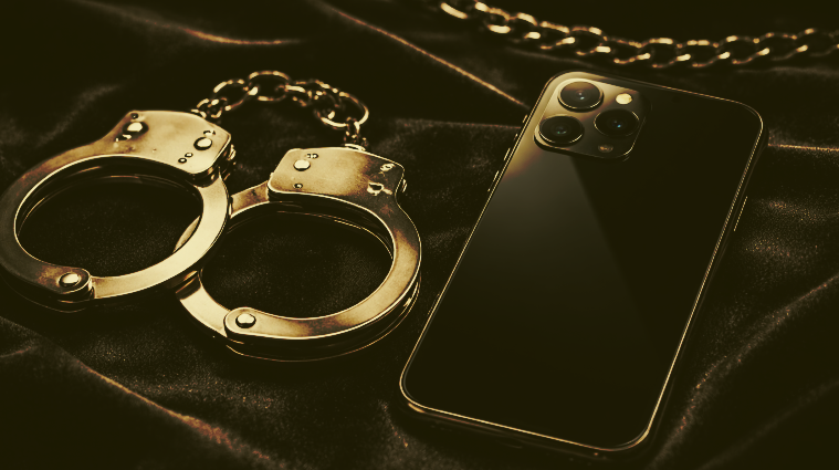 Smartphone y esposas metálicas sobre superficie de terciopelo oscuro con iluminación dramática, concepto de apps BDSM seguras.