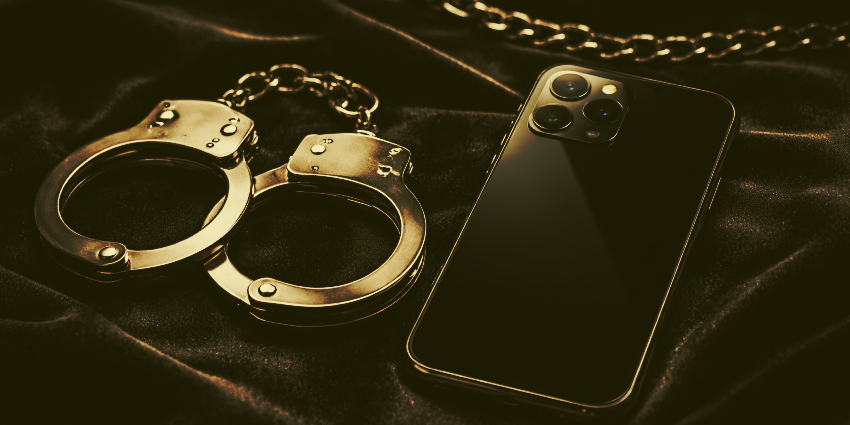 Smartphone y esposas metálicas sobre superficie de terciopelo oscuro con iluminación dramática, concepto de apps BDSM seguras.