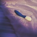 Vibrador ergonómico para el Punto G sobre almohada de satén violeta.