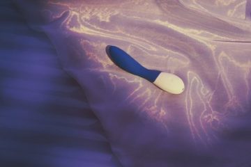 Vibrador ergonómico para el Punto G sobre almohada de satén violeta.