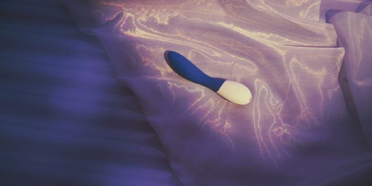 Vibrador ergonómico para el Punto G sobre almohada de satén violeta.