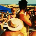 Hombre discutiendo en un chiringuito de playa abarrotado en Maspalomas, con bañistas y sombrillas al fondo bajo el sol.