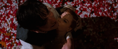 Pareja abrazada entre pétalos rojos en escena íntima de Moulin Rouge