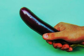 Mano sujetando una berenjena sobre fondo turquesa como metáfora visual del tamaño del pene