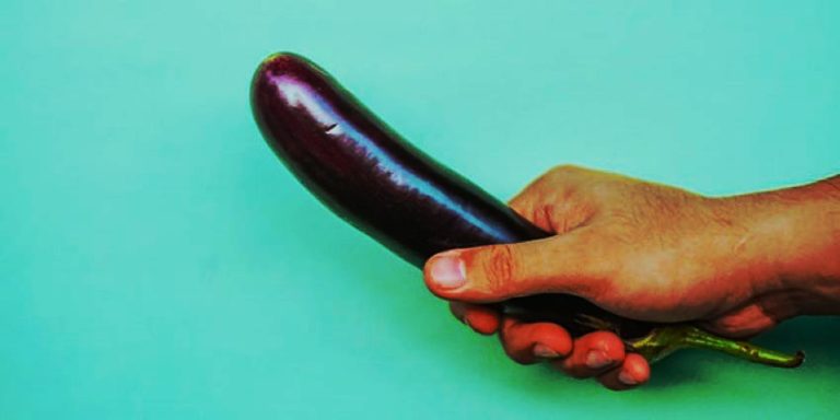 Mano sujetando una berenjena sobre fondo turquesa como metáfora visual del tamaño del pene