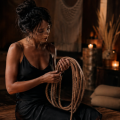 Mujer con vestido negro sosteniendo cuerda de yute en escena de kinbaku con iluminación cálida