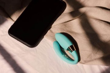 Vibrador para parejas y smartphone sobre una cama, representando la intimidad en las relaciones a distancia mediante tecnología interactiva.