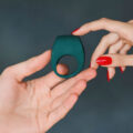 Manos sosteniendo un anillo para el pene de silicona verde oscuro