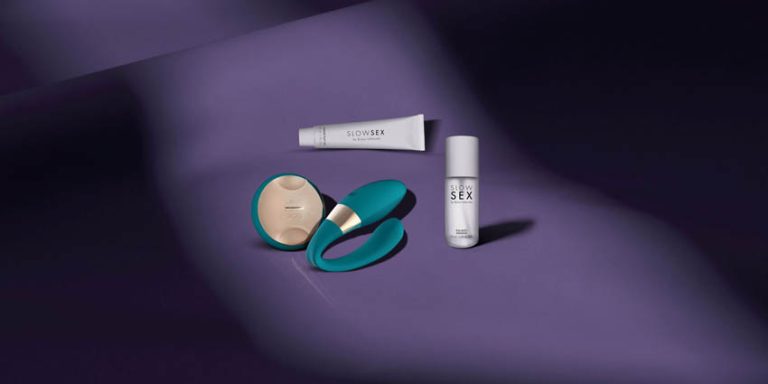 Bodegón de productos de bienestar sexual de la marca LELO y Slow Sex sobre un fondo púrpura suave, incluyendo un vibrador ergonómico de color turquesa, un estimulador circular y productos de cosmética íntima, diseñados para la comodidad y la accesibilidad.