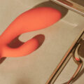 Vibrador conejo coral sobre una superficie beige iluminada por luz natural