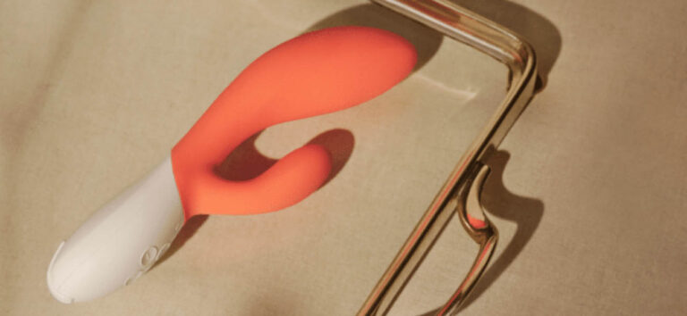 Vibrador conejo coral sobre una superficie beige iluminada por luz natural