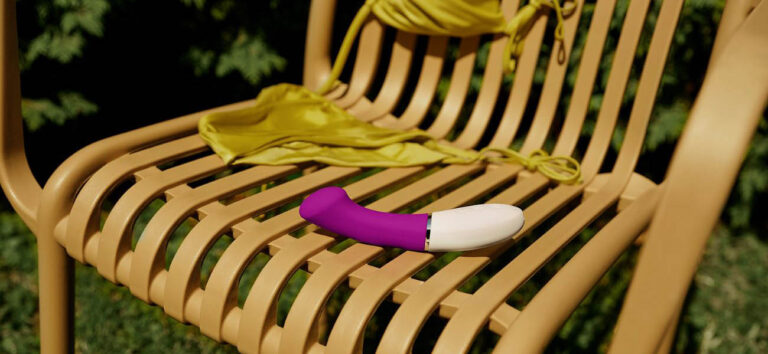 Vibrador tipo dildo curvado sobre una tumbona de exterior para ilustrar cómo elegir el tamaño adecuado