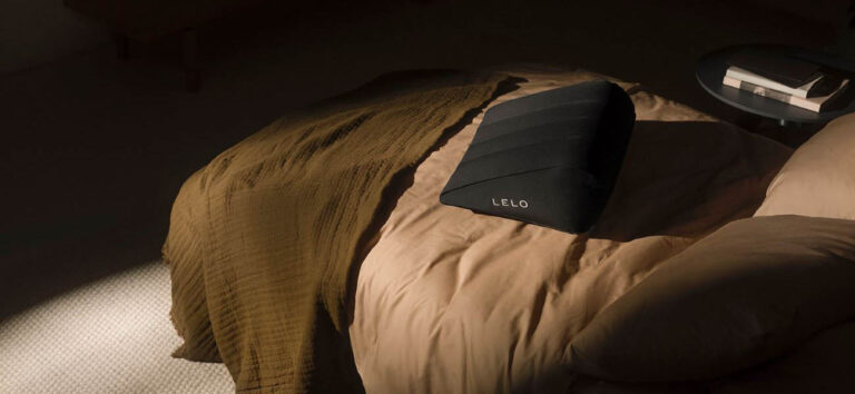 Almohada sexual hinchable de LELO colocada sobre una cama en un dormitorio elegante y discreto